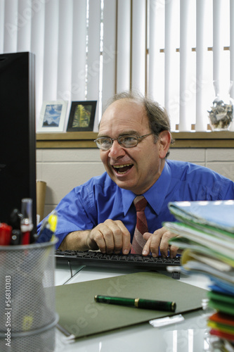Businessman laughing while looking at computer monitor, vertical