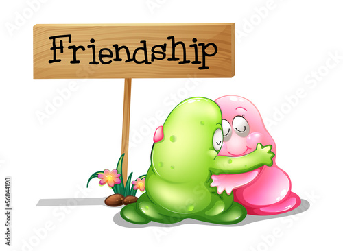 A green and a pink monster hugging near the wooden signage
