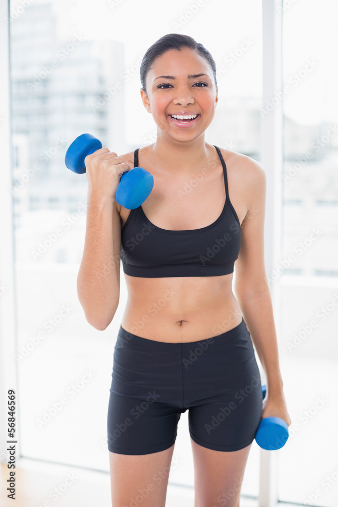 Laughing dark haired model in sportswear exercising with dumbbel