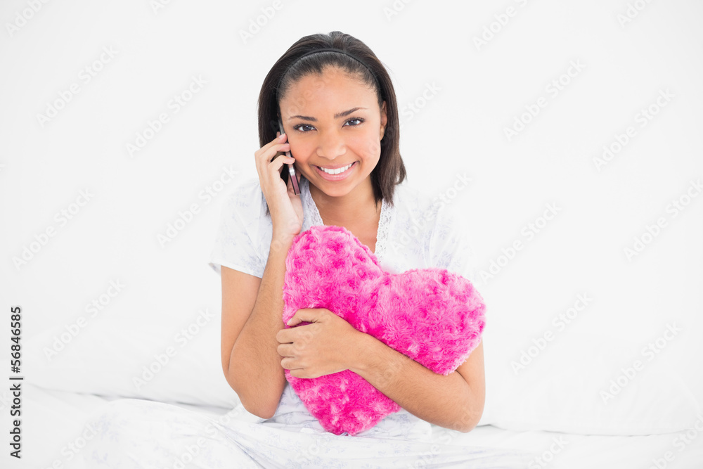 Smiling young dark haired model holding a pillow and making a ph Smiling young dark haired model holding a pillow and making a ph