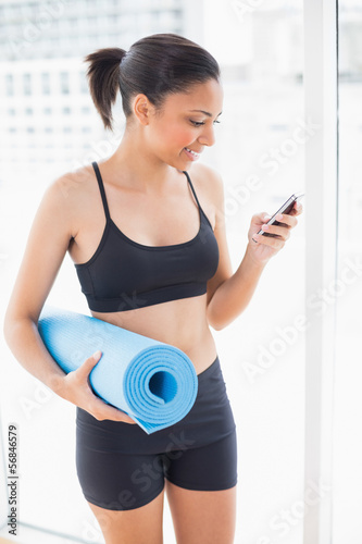 Pleased dark haired model in sportswear carrying an exercise mat © lightwavemedia