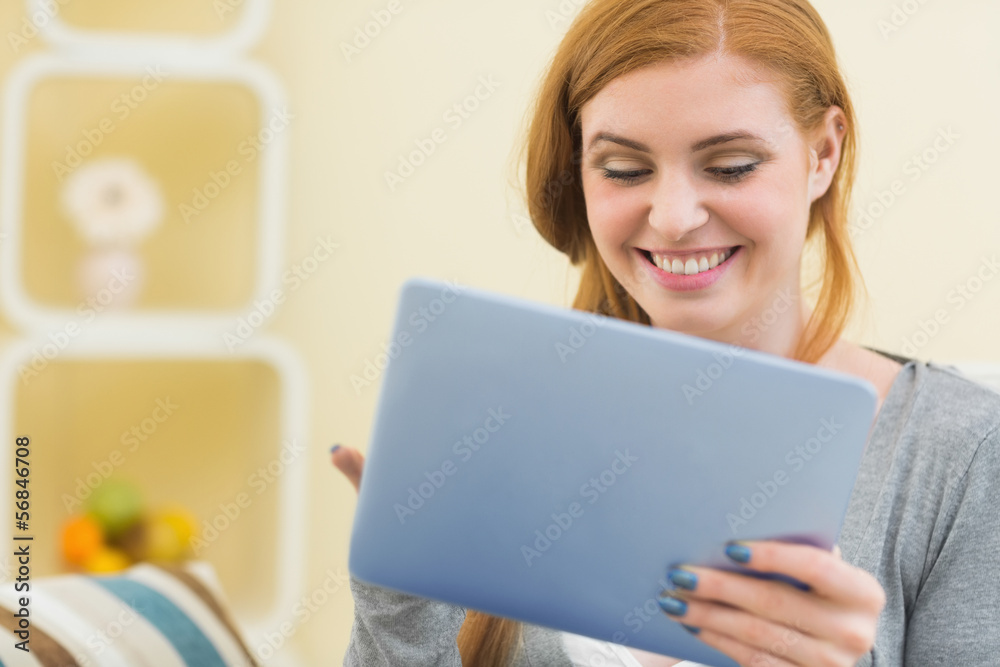 Smiling redhead sitting on the couch using tablet Smiling redhead sitting on the couch using tablet