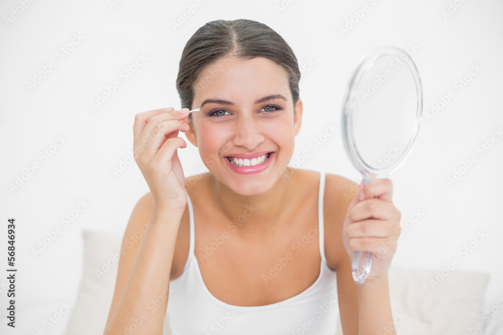 Amused young brown haired model in white pajamas plucking her ey Amused young brown haired model in white pajamas plucking her ey