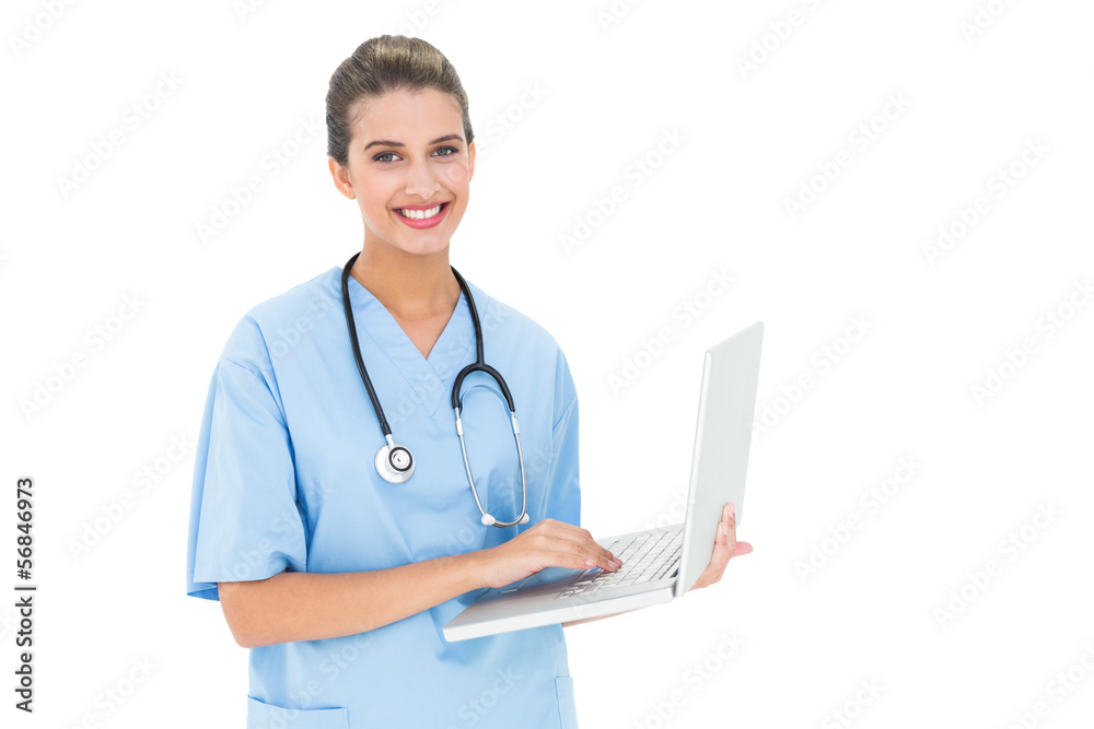 Cheerful brown haired nurse in blue scrubs using a laptop Cheerful brown haired nurse in blue scrubs using a laptop