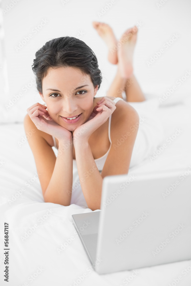 Content casual brunette in white pajamas lying on her bed and lo Content casual brunette in white pajamas lying on her bed and lo