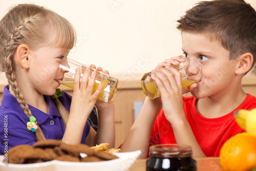 Two kids drink orrange juice while looking on each other