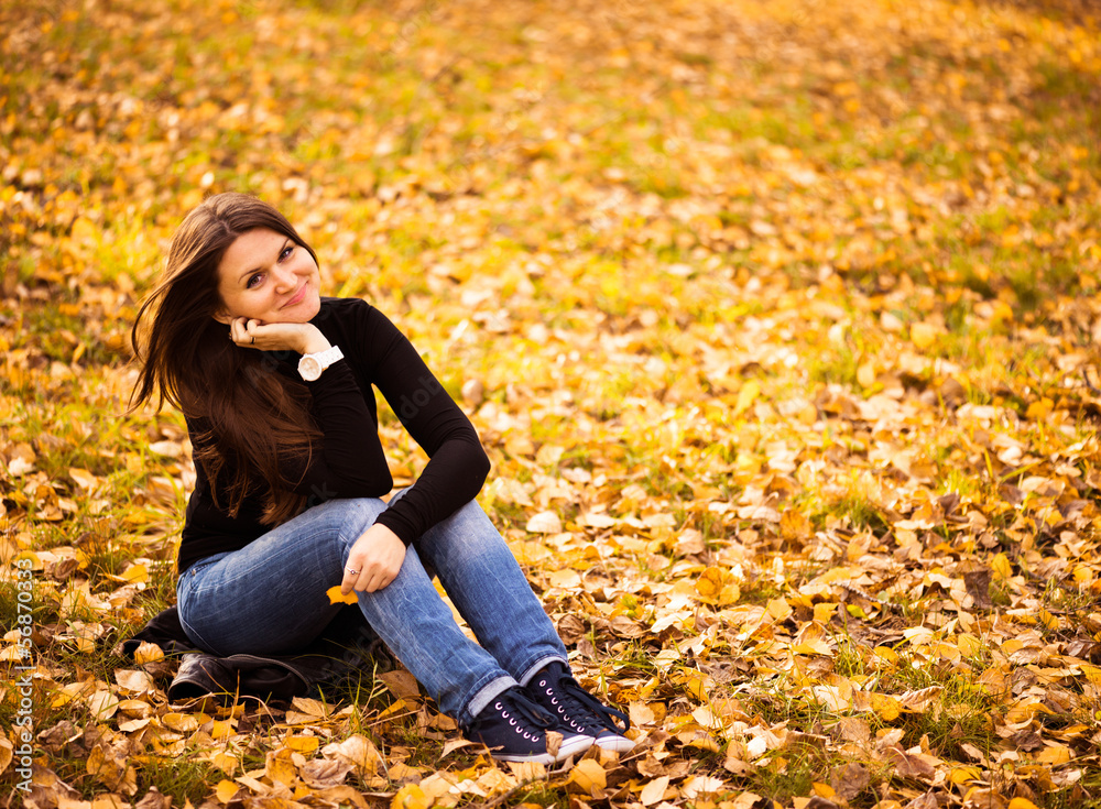 young woman sits on leaves in autumn park