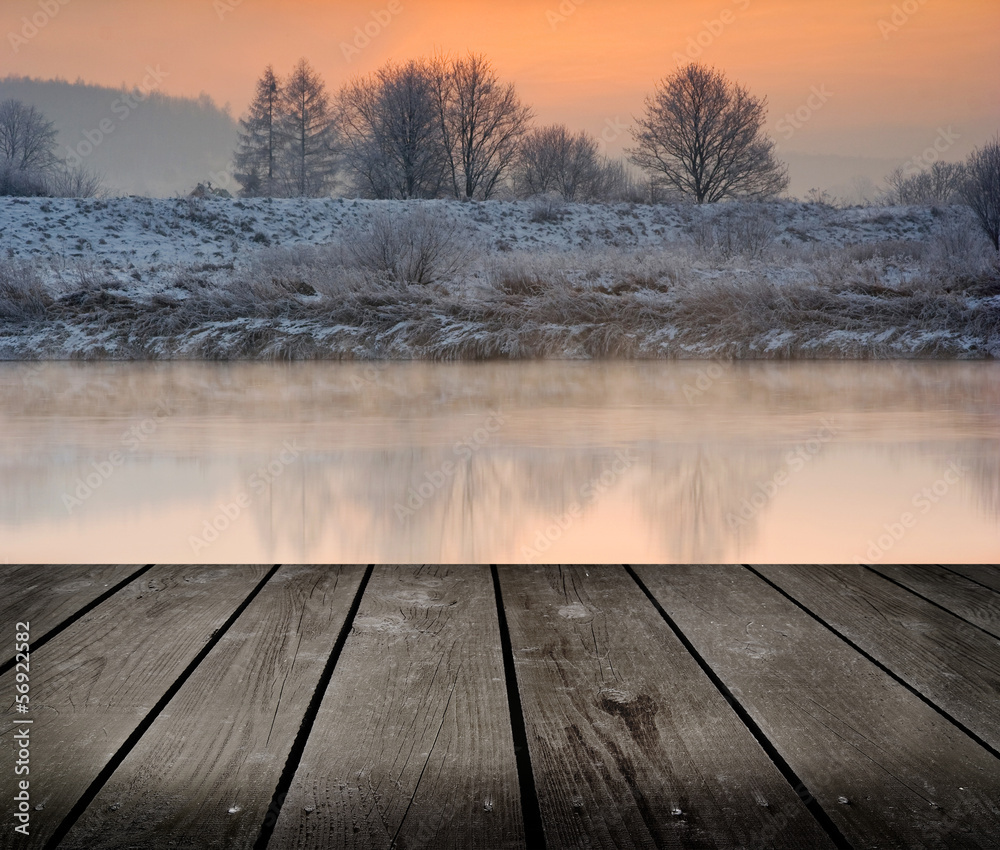 Winter sunrise over the river and empty wooden deck table.