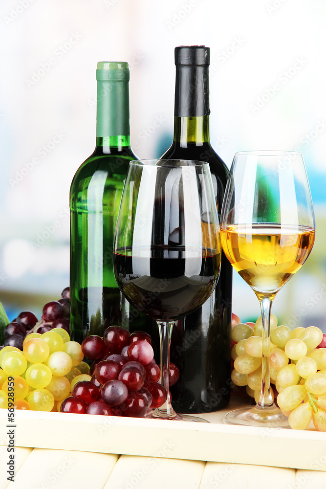 Fototapeta premium Wine bottles and glasses of wine on tray, on bright background