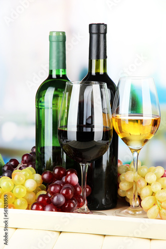 Wine bottles and glasses of wine on tray, on bright background