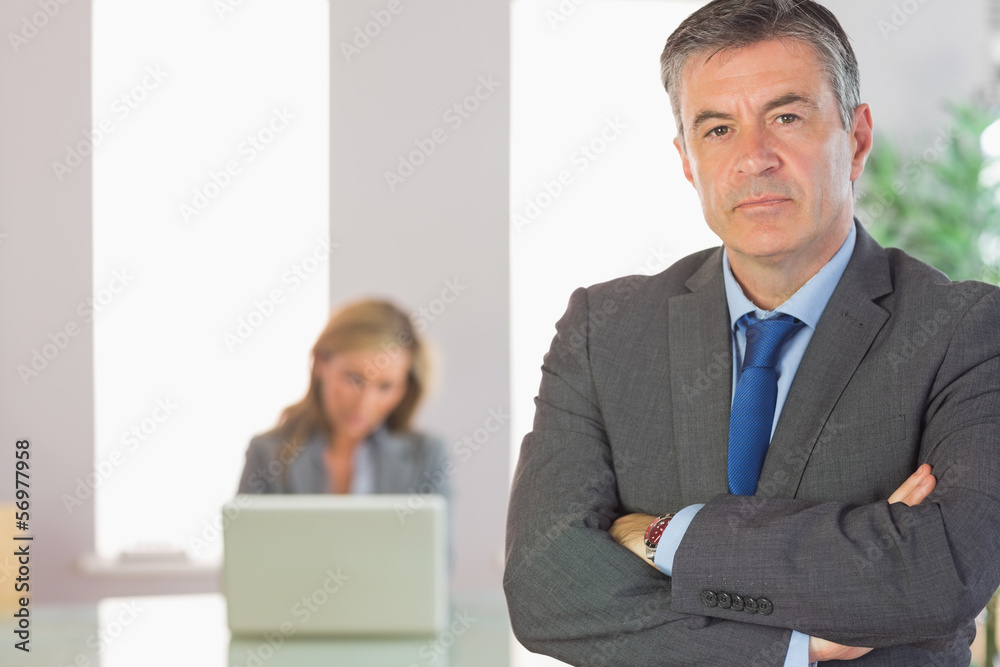 Unsmiling businessman looking at camera crossed arms with a busi Unsmiling businessman looking at camera crossed arms with a busi