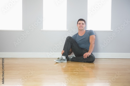 Smiling handsome man leaning against wall sitting on the floor