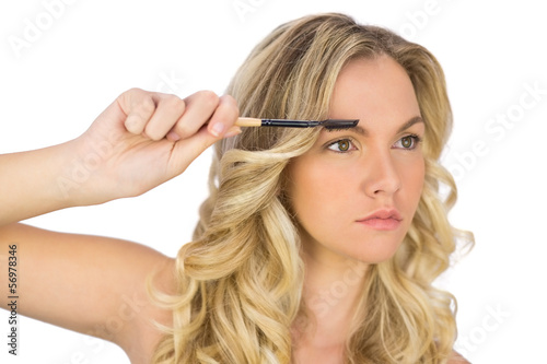 Thoughtful curly haired blonde using eyebrow brush