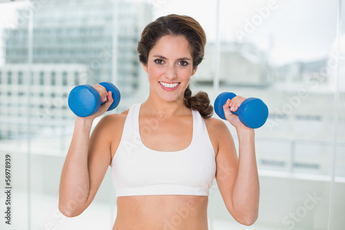 Sporty smiling brunette holding dumbbells