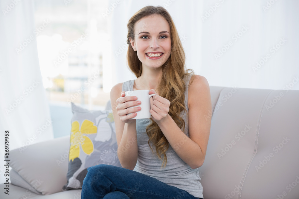 Happy young woman sitting on sofa holding a mug Happy young woman sitting on sofa holding a mug