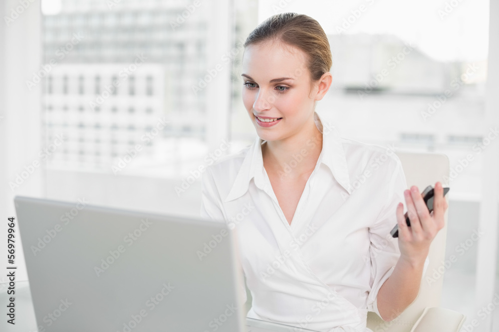Cheerful businesswoman using laptop and texting on smartphone Cheerful businesswoman using laptop and texting on smartphone