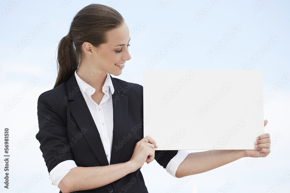 Young businesswoman holding blank sign against blue sky Young businesswoman holding blank sign against blue sky