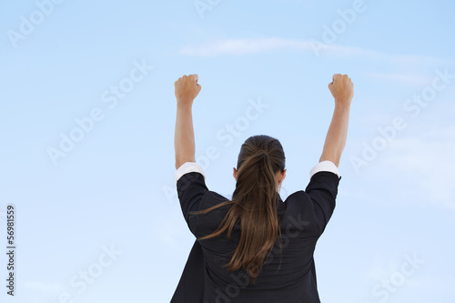 Slika na platnu Businesswoman with arms up against blue sky, rear view