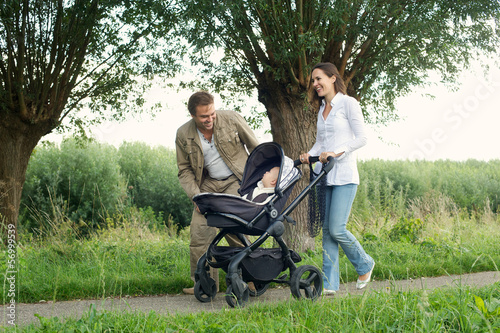 Happy mother and father walking outdoors with baby in pram