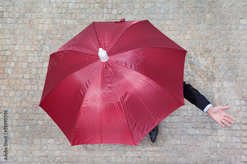 Businessman hidden under umbrella and checking if it's raining
