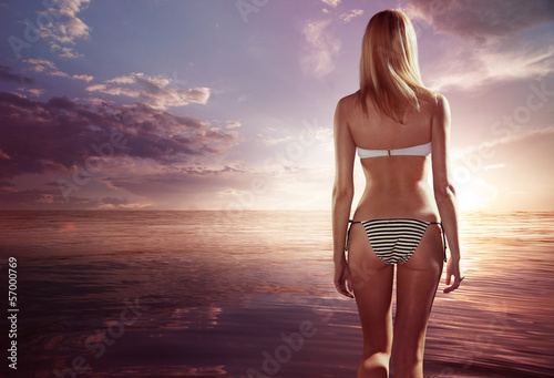 Young woman in bikini standing and looking on sunset