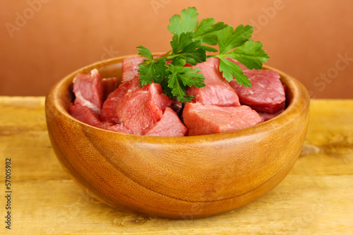 Raw beef meat in bowl on wooden table on brown background