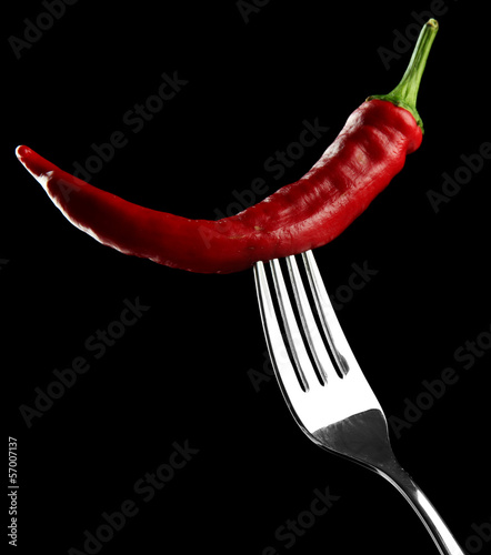 Red hot chili pepper on fork, isolated on black