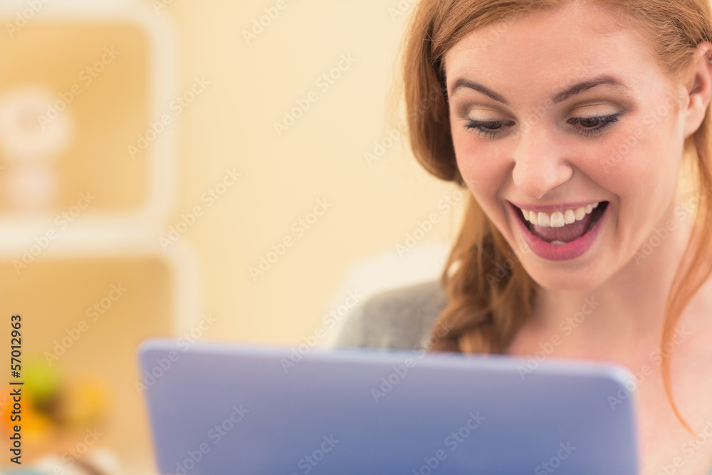 Laughing redhead sitting on the couch using tablet pc Laughing redhead sitting on the couch using tablet pc