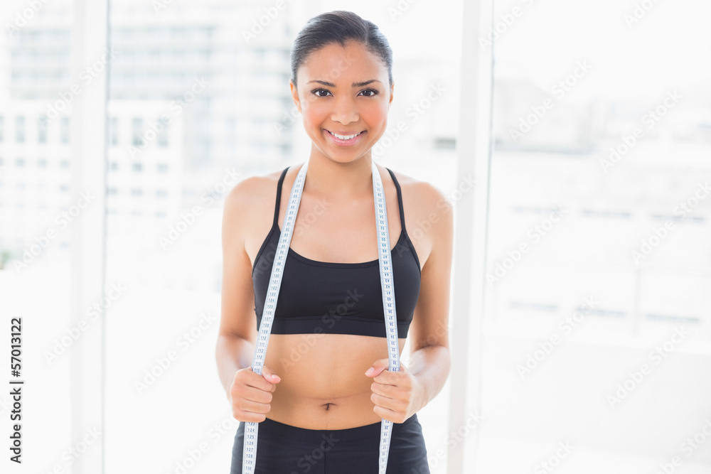 Smiling dark haired model in sportswear holding a measuring tape