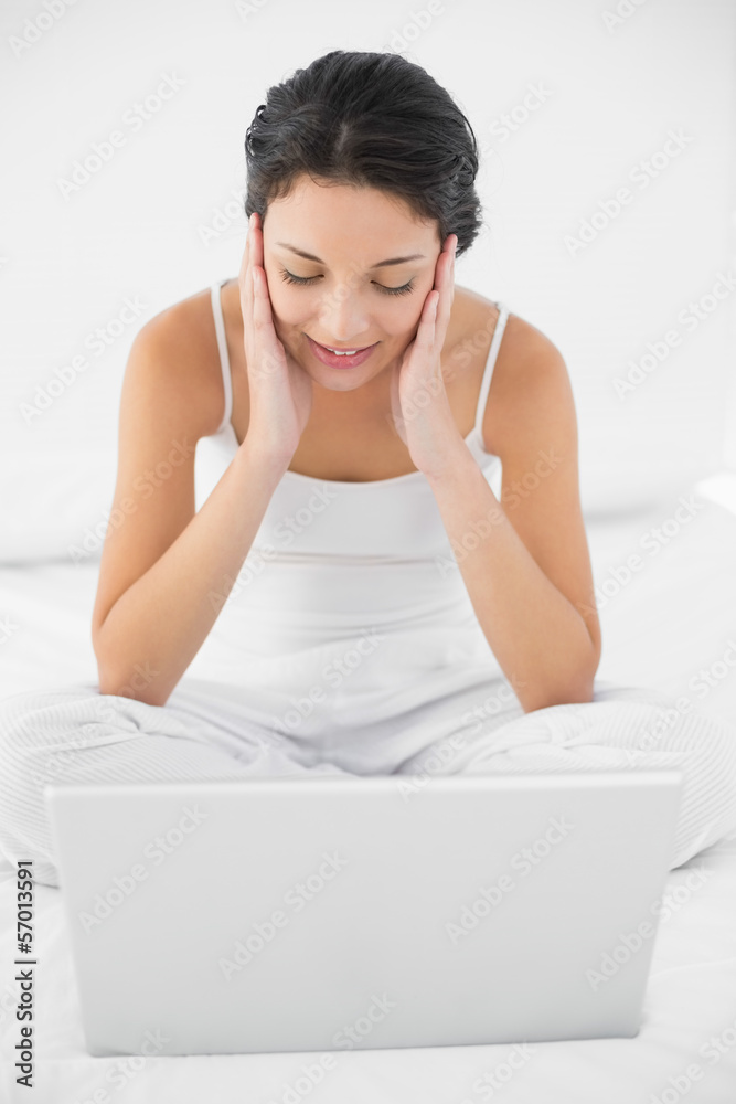 Dreamy casual brunette in white pajamas sitting on her bed and l