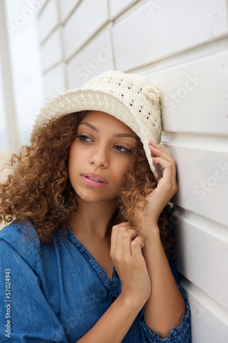 Beautiful young woman wearing hat and leaning against wall