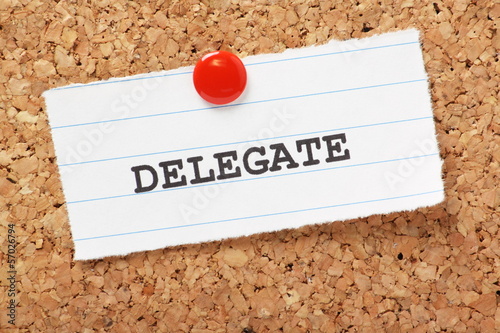 The word Delegate on paper note pinned to a cork notice board