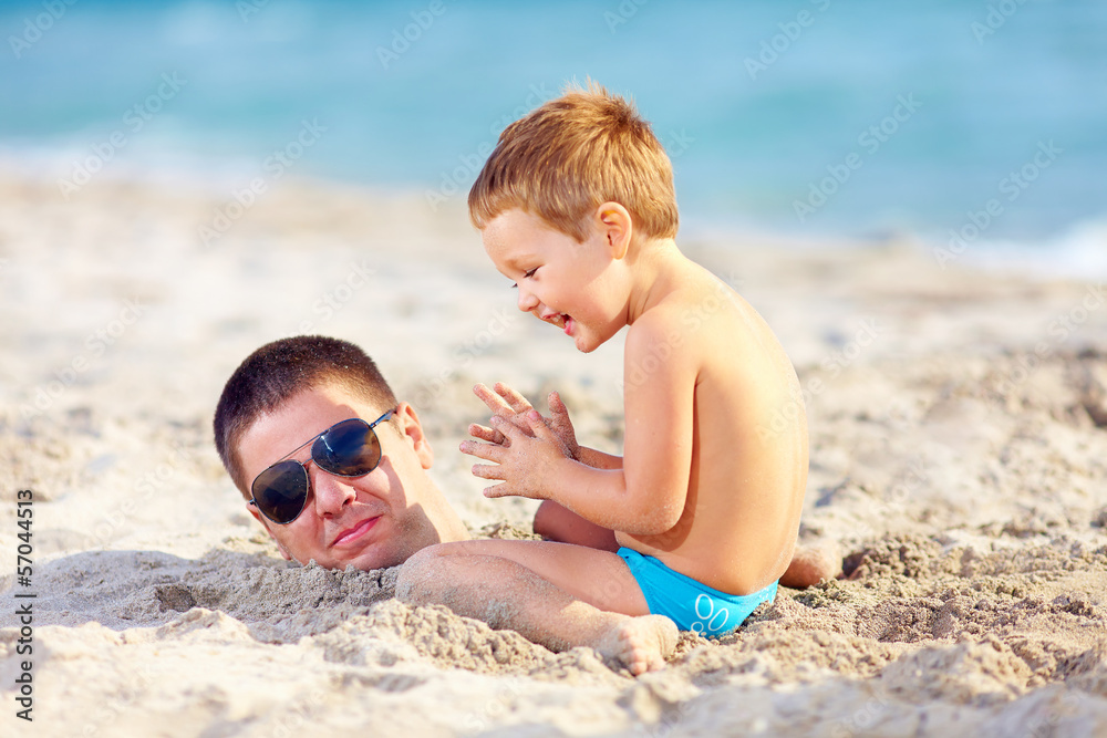 father and son having fun in sand on the beach father and son having fun in sand on the beach