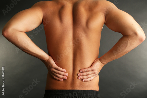 Young man with back pain on grey background