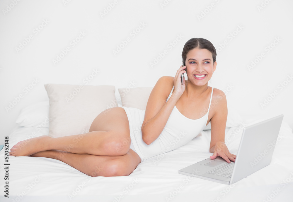 Charming young brown haired model in white pajamas making a phon Charming young brown haired model in white pajamas making a phon