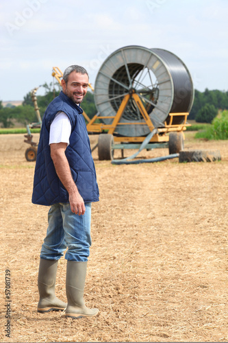 Famer stood in field machinery in background photo