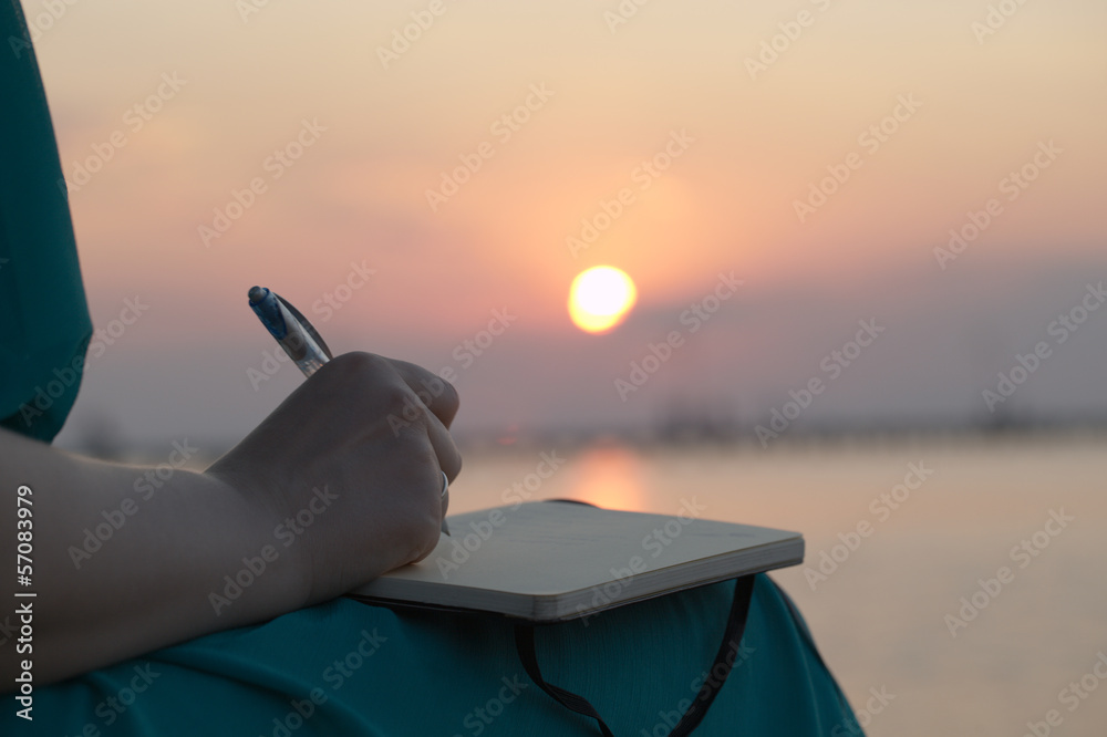 Fototapeta premium Woman writing in her diary at sunset