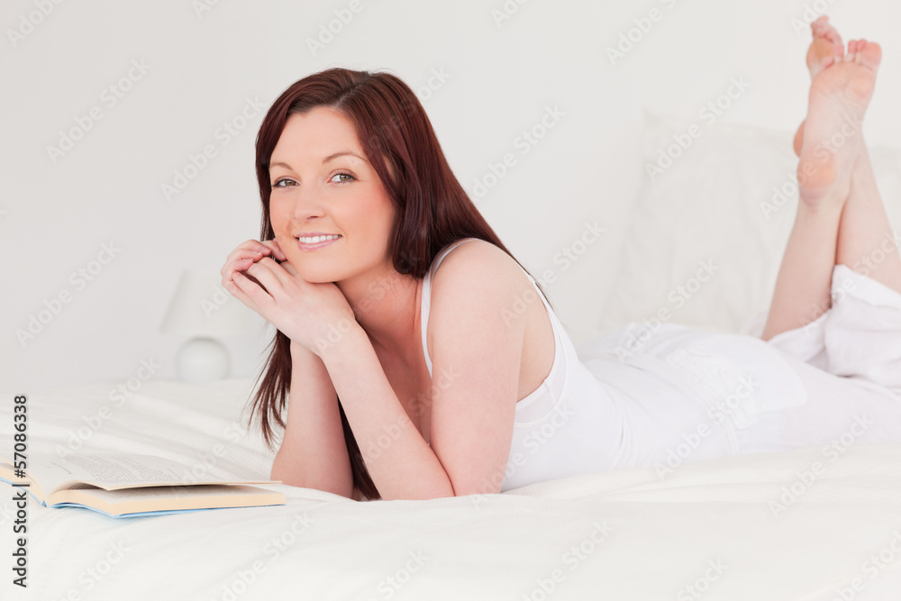 Attractive red-haired woman reading a book while lying on her be Attractive red-haired woman reading a book while lying on her be