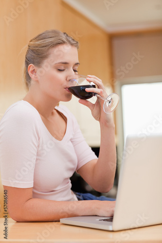 Portrait of a young woman using a laptop while drinking red wine