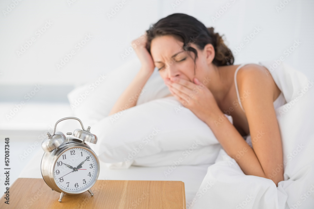 Tired casual brunette in white pajamas lying in her bed and yawn Tired casual brunette in white pajamas lying in her bed and yawn