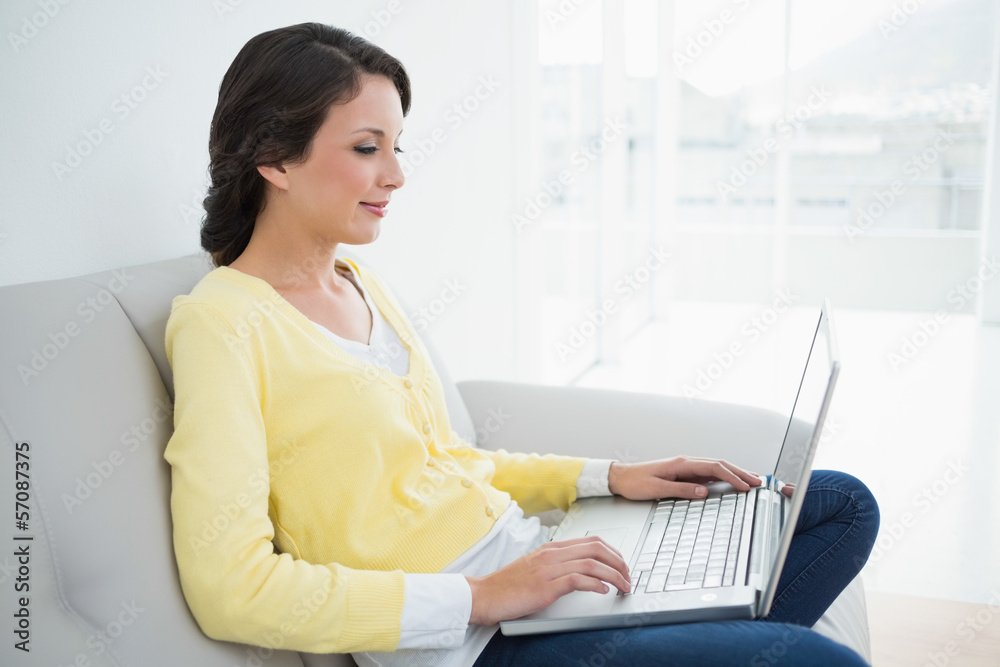 Charming casual brunette in yellow cardigan typing on a laptop Charming casual brunette in yellow cardigan typing on a laptop