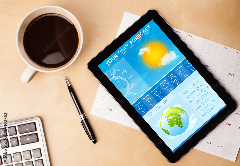 Tablet pc showing weather forecast on screen with a cup of coffe Tablet pc showing weather forecast on screen with a cup of coffe