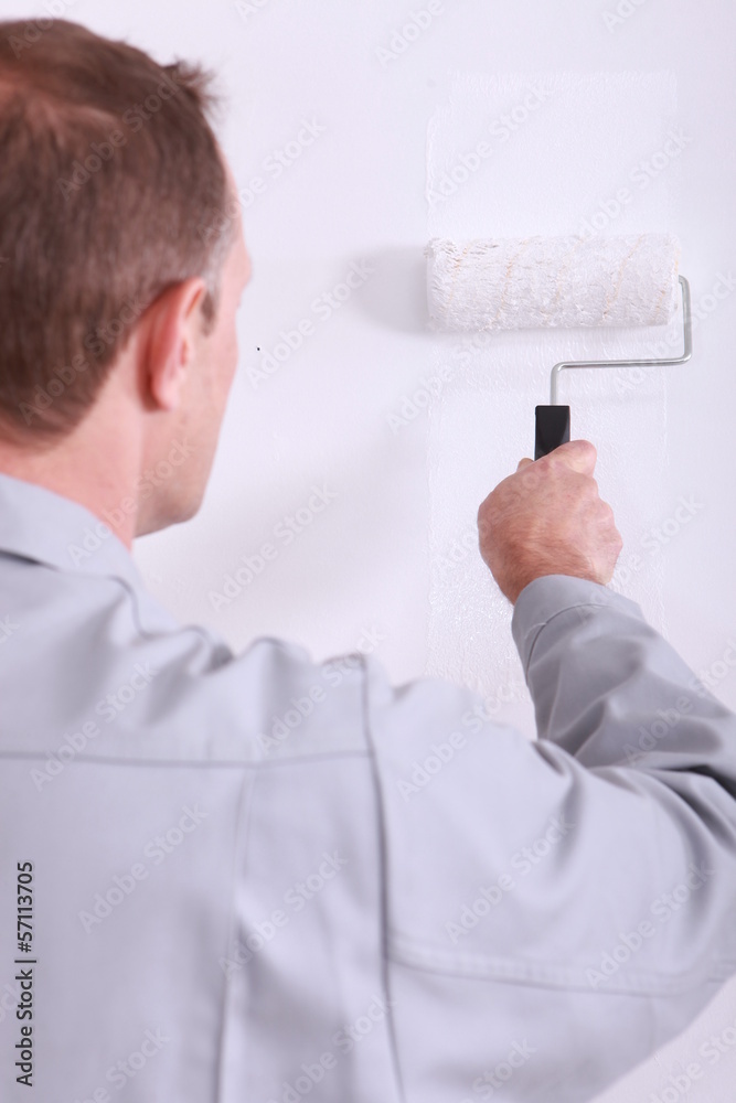 Man painting a wall white with a roller Man painting a wall white with a roller