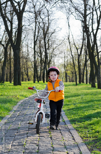 Fototapeta Naklejka Na Ścianę i Meble -  Little boy pushing his bicycle in a park