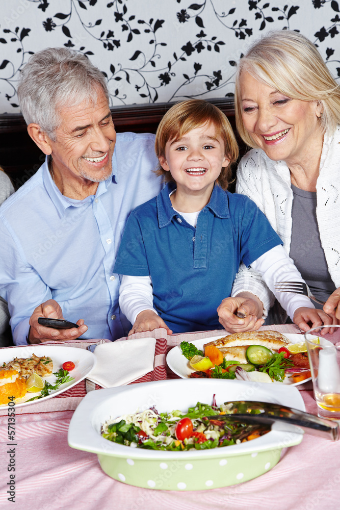Lachendes Kind isst mit Großeltern