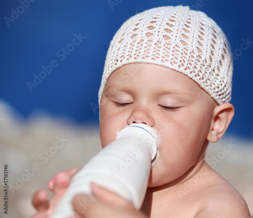 Little baby drinks milk from the white plastic bottle