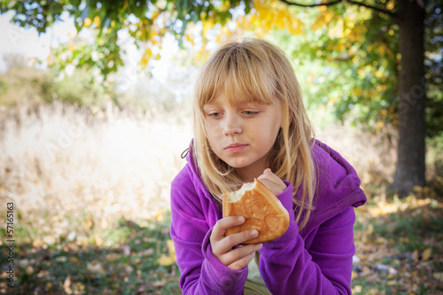 Little blond girl on a picnic in autumn park eats pies