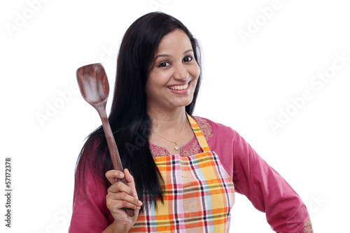 Young Indian woman holding kitchen utensil against white
