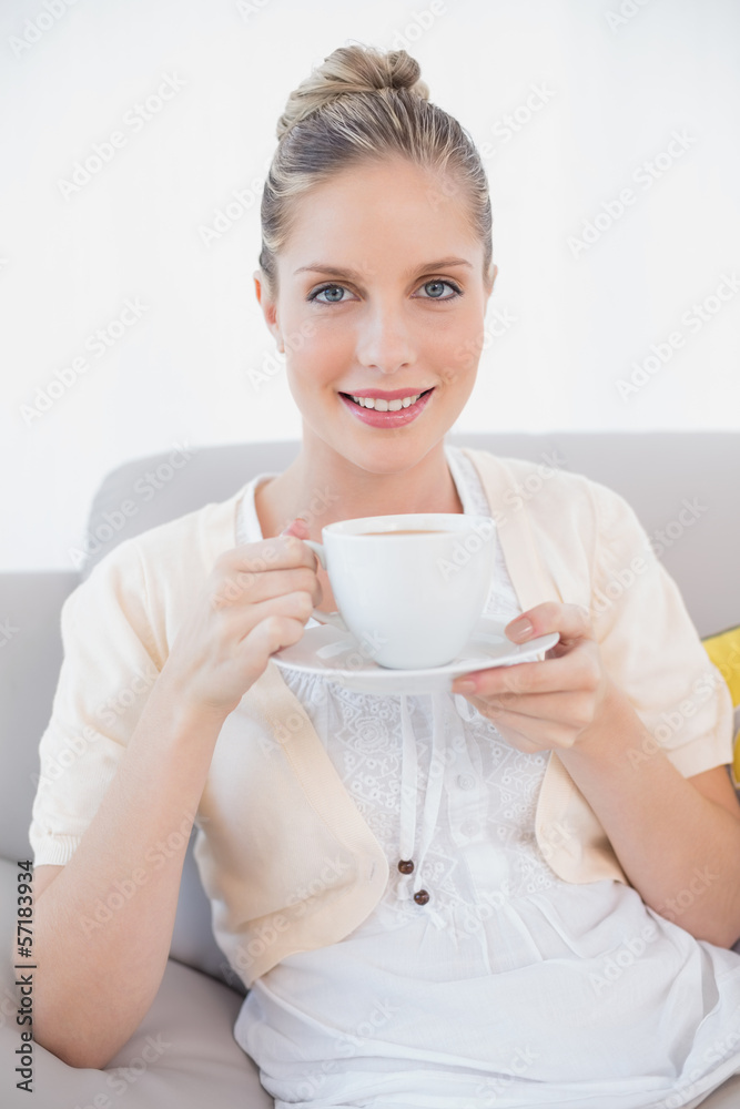 Smiling fresh model holding coffee sitting on sofa Smiling fresh model holding coffee sitting on sofa
