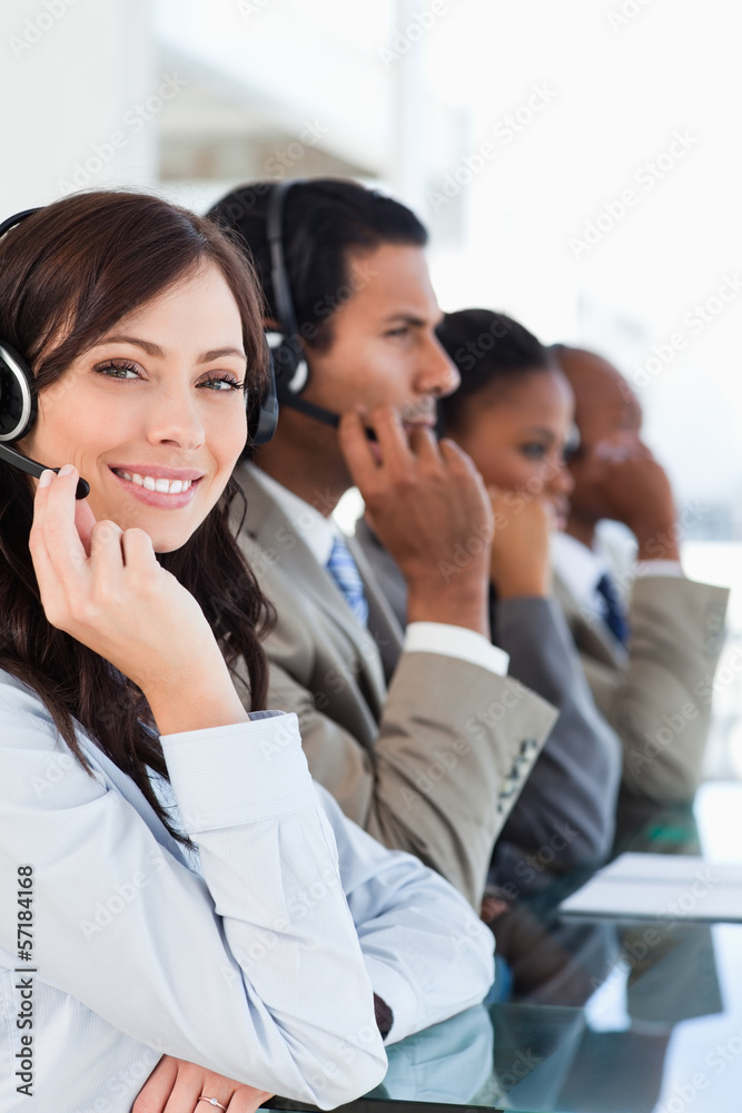 Smiling call centre agent looking at the camera while working ha Smiling call centre agent looking at the camera while working ha